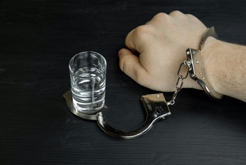 A hand in handcuffs to a glass of alcohol -symbolising addiction and loss of control in a binge drinking story
